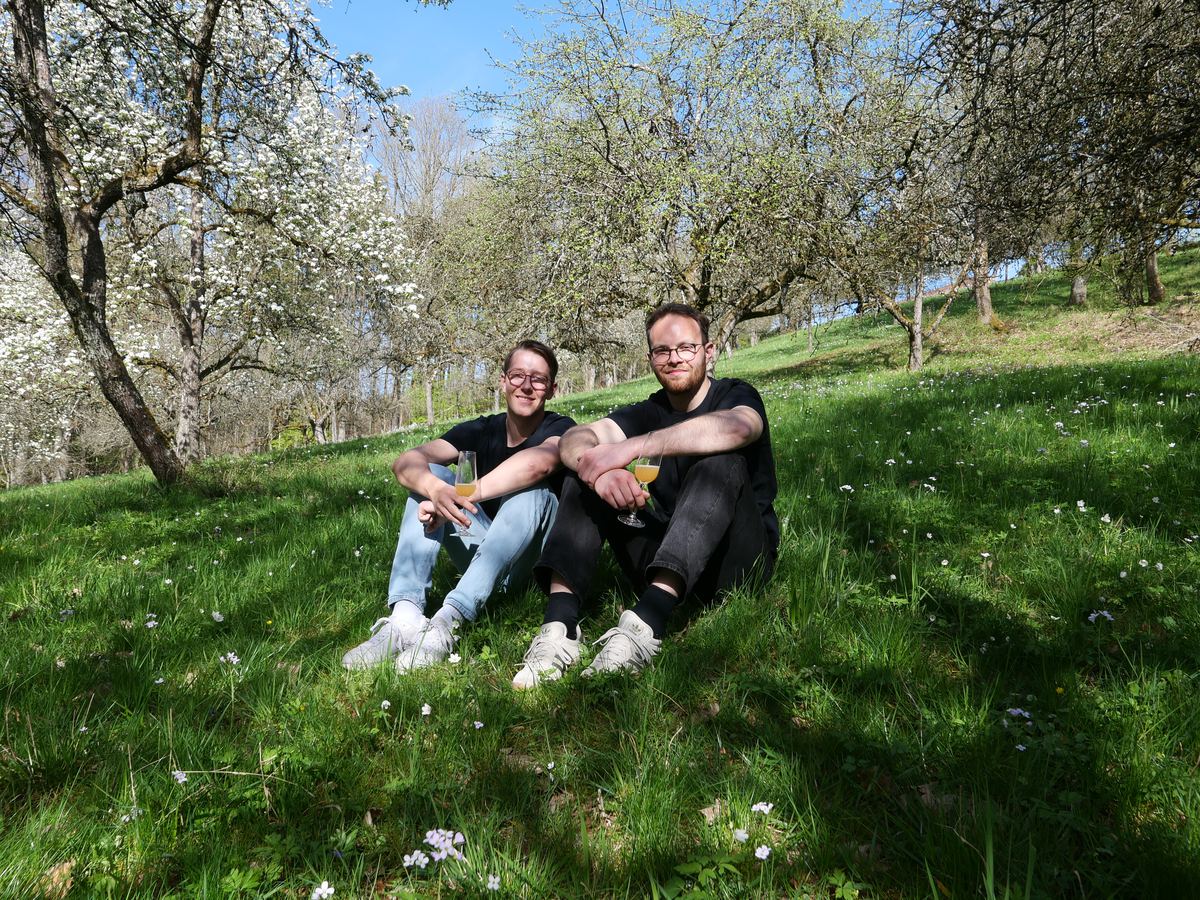 Nick und Max sitzen auf einer Streuobstwiese mit Cider-Gläsern