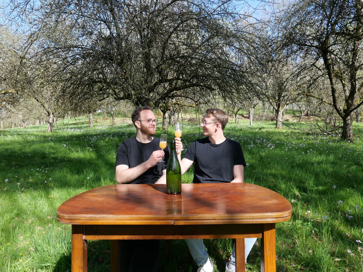 Nick und Max stoßen mit Cider an einem Tisch auf der Streuobstwiese an